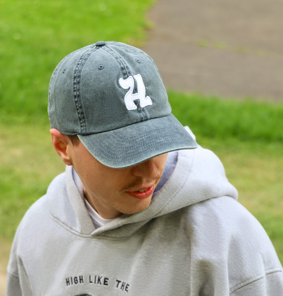 Czapka z daszkiem na modelu. W klimacie vintage. Czapka z białym haftem litery H, jeansowy materiał, styl streetwear