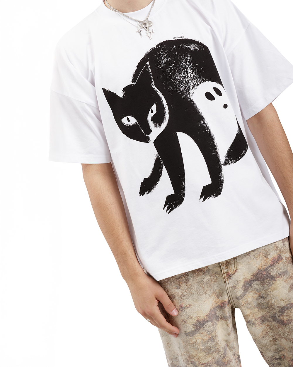 Zbliżenie na koszulkę z kotem – biały t-shirt oversize z czarną grafiką kota, w którego cieniu ukryty jest duch. Model w marmurkowych spodniach i naszyjnikach. Nowoczesny design z motywem kota, idealny do stylizacji streetwear i artystycznych outfitów.