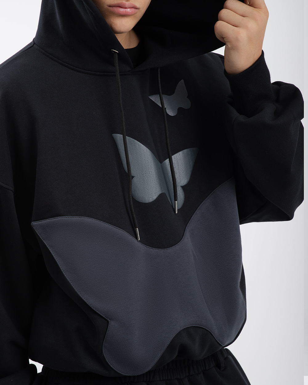 Model w czarnej bluzie z motylem, widoczna funkcjonalna kieszeń w kształcie motyla oraz puff print nad nią, ujęcie na górną część bluzy