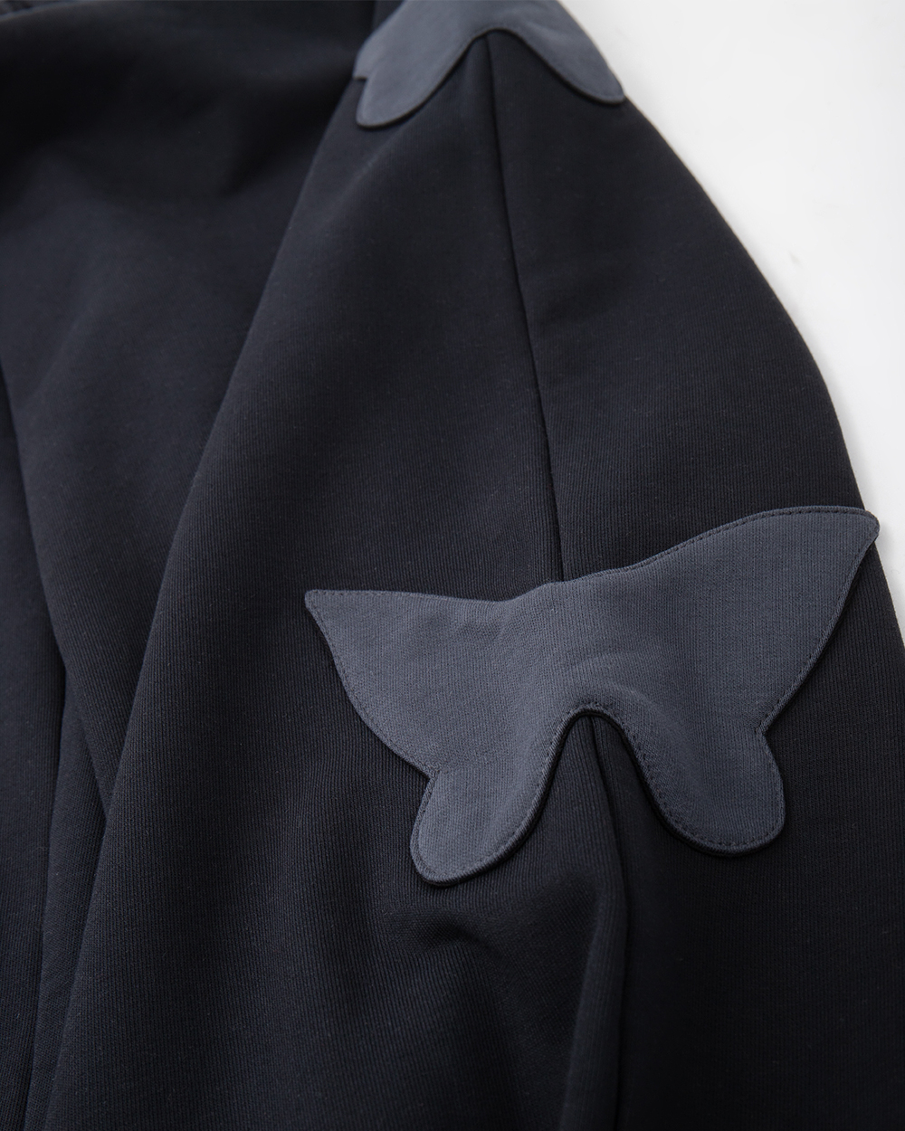 Zbliżenie na boczną naszywkę w kształcie motyla na spodniach dresowych baggy, widoczna struktura materiału i szew nogawki