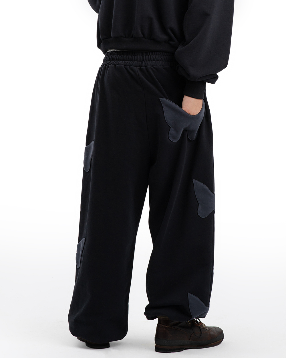 Tył spodni dresowych baggy na modelu, widoczne naszywki w kształcie motyli na nogawkach i luźny, szeroki krój