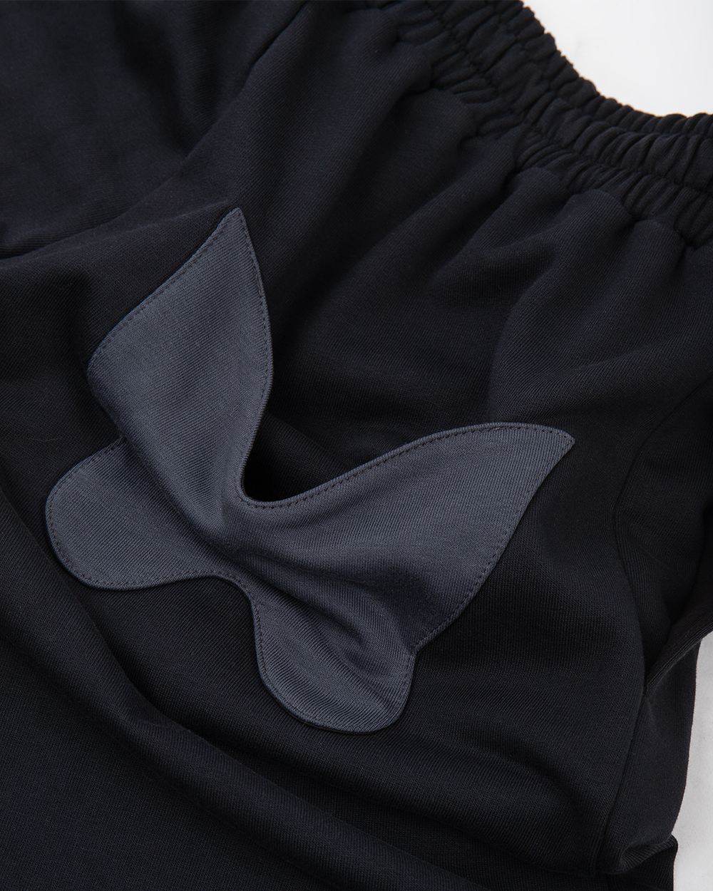 Kieszeń w kształcie motyla na tyle spodni dresowych baggy, zbliżenie na naszywkę i strukturę materiału