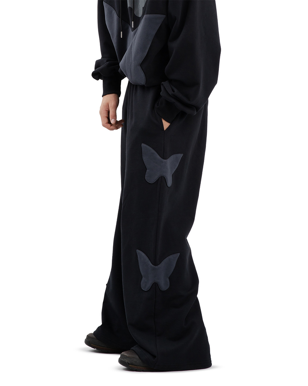 Spodnie dresowe baggy na modelu, boczny widok z widocznymi naszywkami w kształcie motyli na nogawkach i luźnym krojem